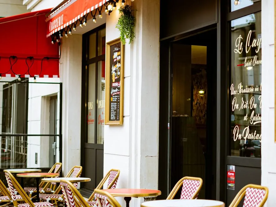 Terrasse de brasserie avec tables rondes, chaises bistrot et store rouge